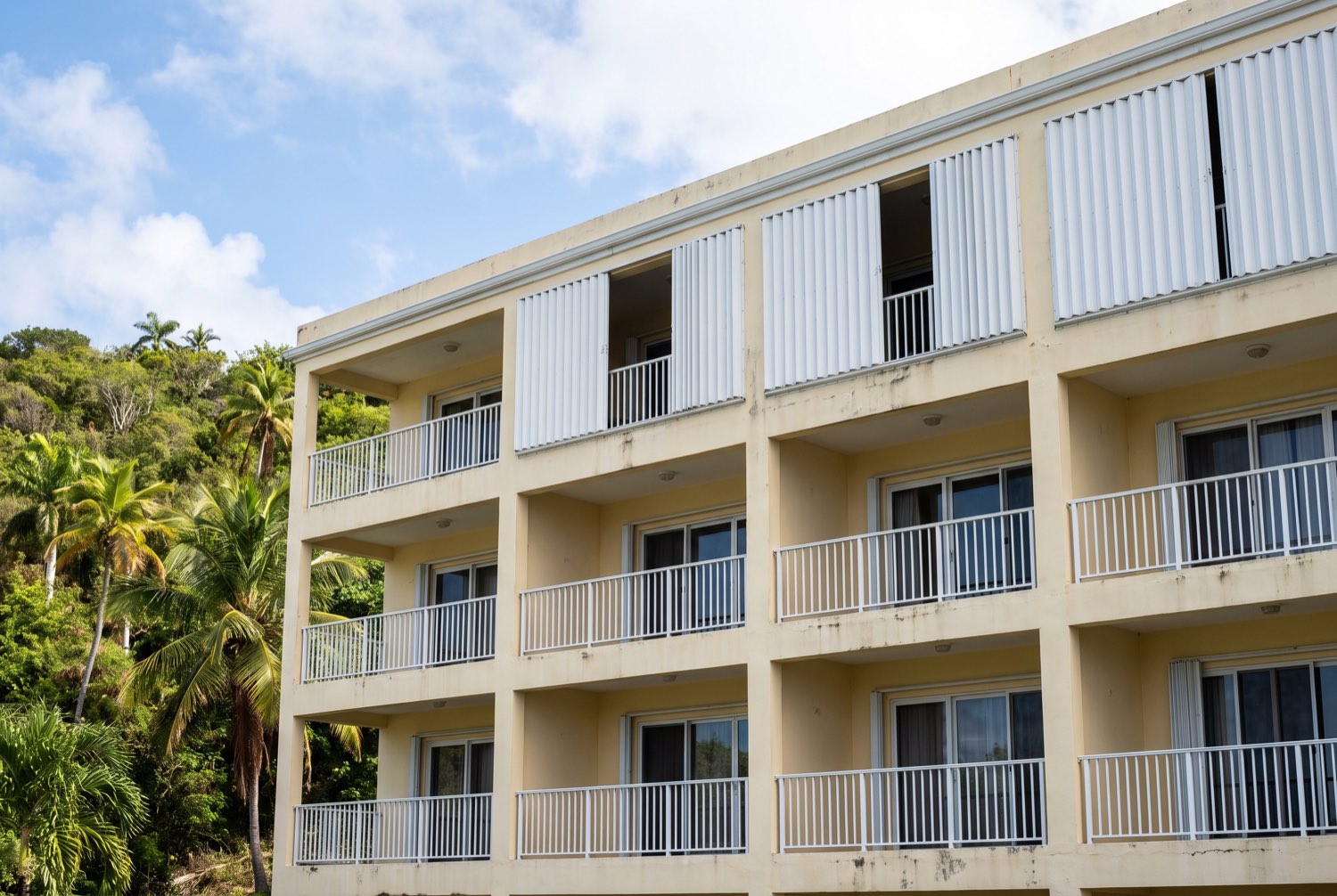 A Caribbean condominium building with white accordion storm shutters fitted to every balcony opening.